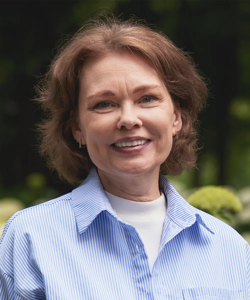 A smiling woman in her 50s with shoulder-length hair, wearing a striped shirt