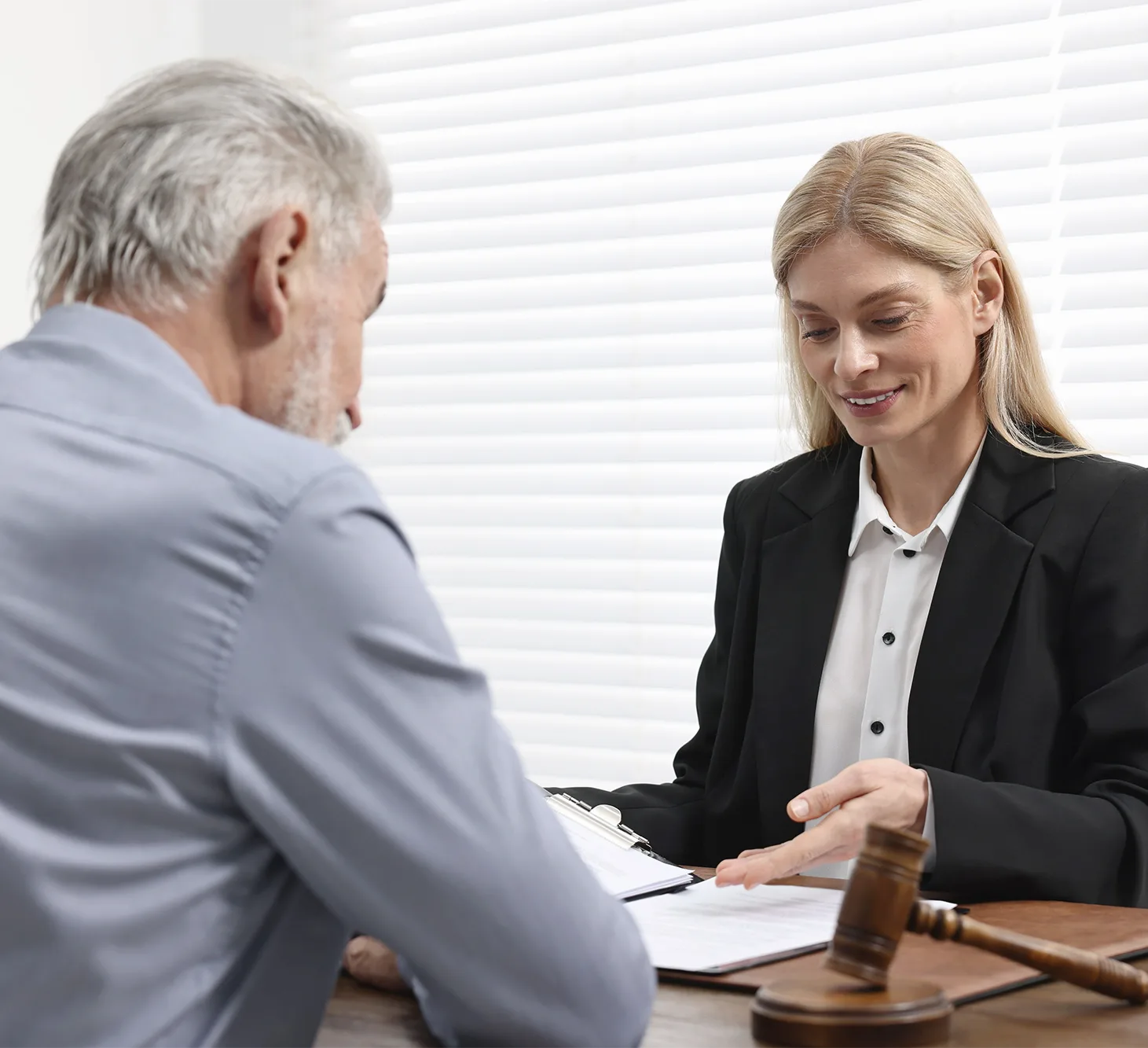 A representative reviews documents with an older man across a desk with a gavel