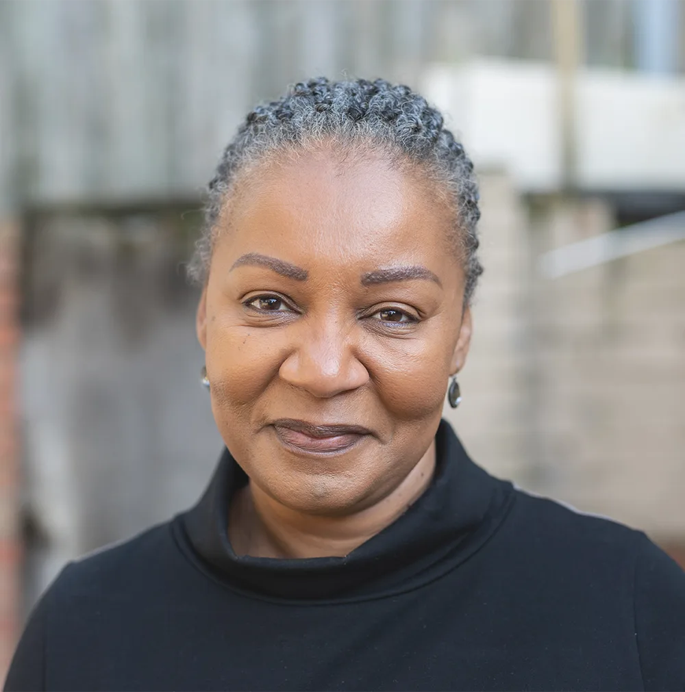 A smiling woman in her early 60s with gray braided hair, wearing a black top