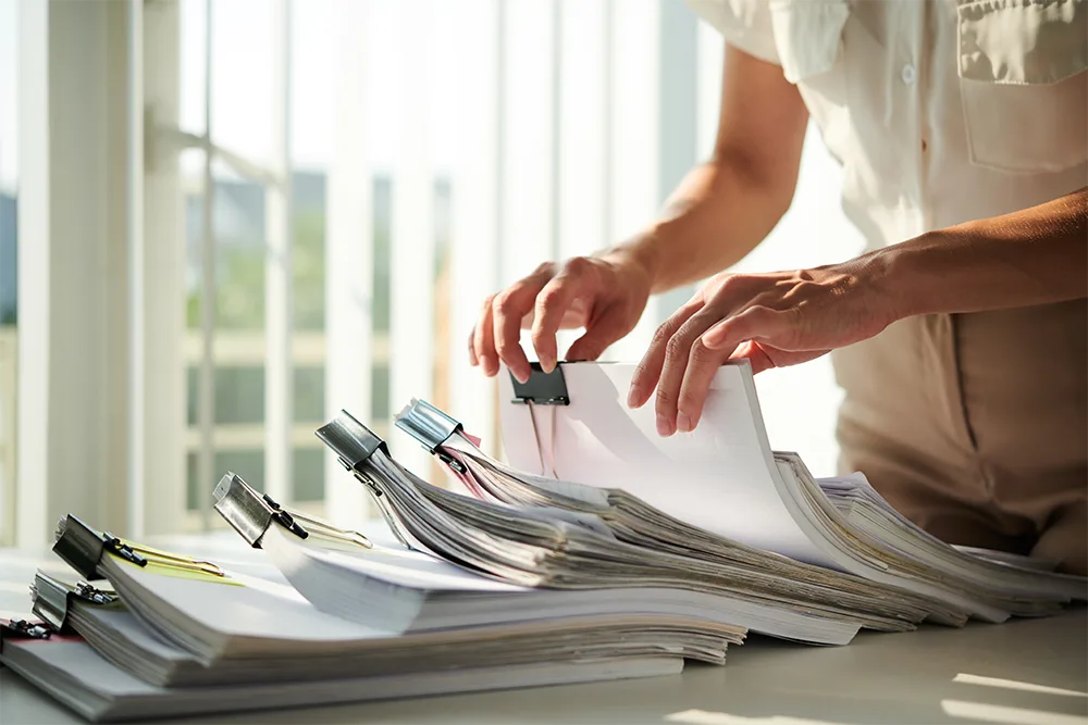 Hands sorting through stacks of clipped documents and records on a desk